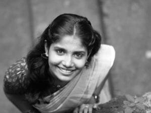 Black and white portrait of a smiling woman in a saree looking up.